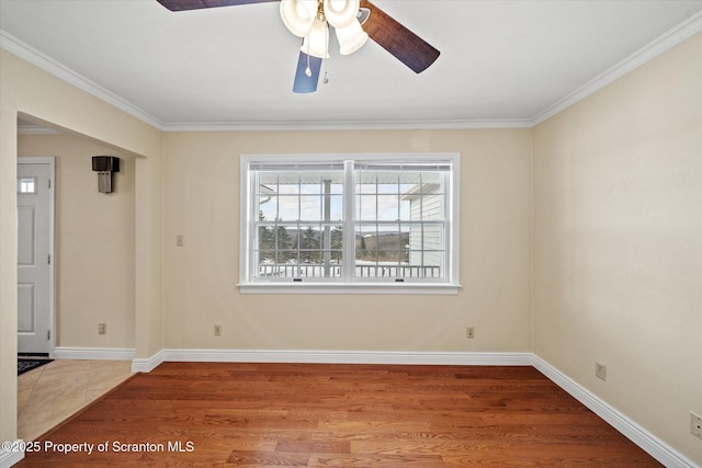 empty room with ornamental molding, wood finished floors, a ceiling fan, and baseboards