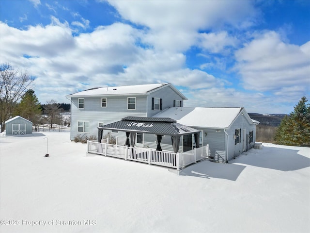 snow covered rear of property featuring a storage shed, a porch, and an outdoor structure