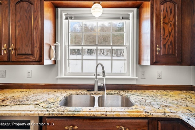 kitchen with a sink, dark brown cabinetry, and light stone countertops