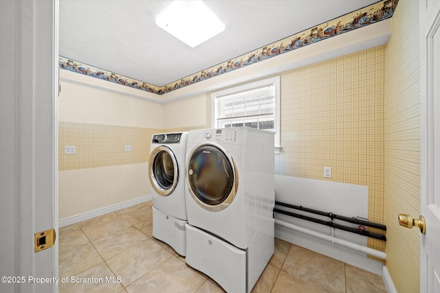 laundry room featuring tile walls, laundry area, light tile patterned flooring, and washer and clothes dryer