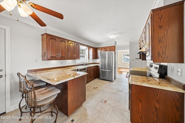 kitchen with a peninsula, a sink, appliances with stainless steel finishes, brown cabinets, and plenty of natural light