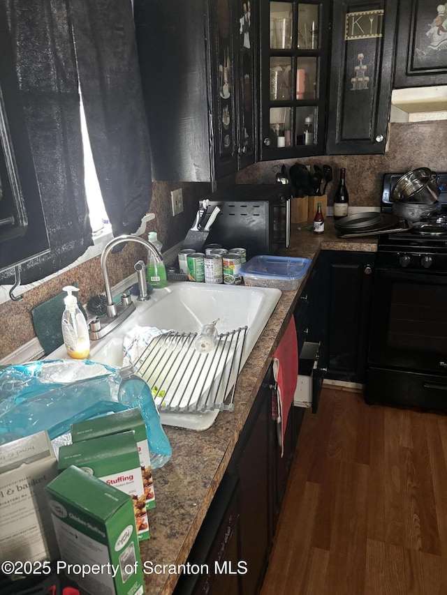 kitchen with under cabinet range hood, dark cabinets, black range with gas cooktop, a sink, and glass insert cabinets