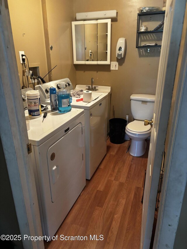 half bathroom featuring washing machine and dryer, toilet, wood finished floors, and a sink
