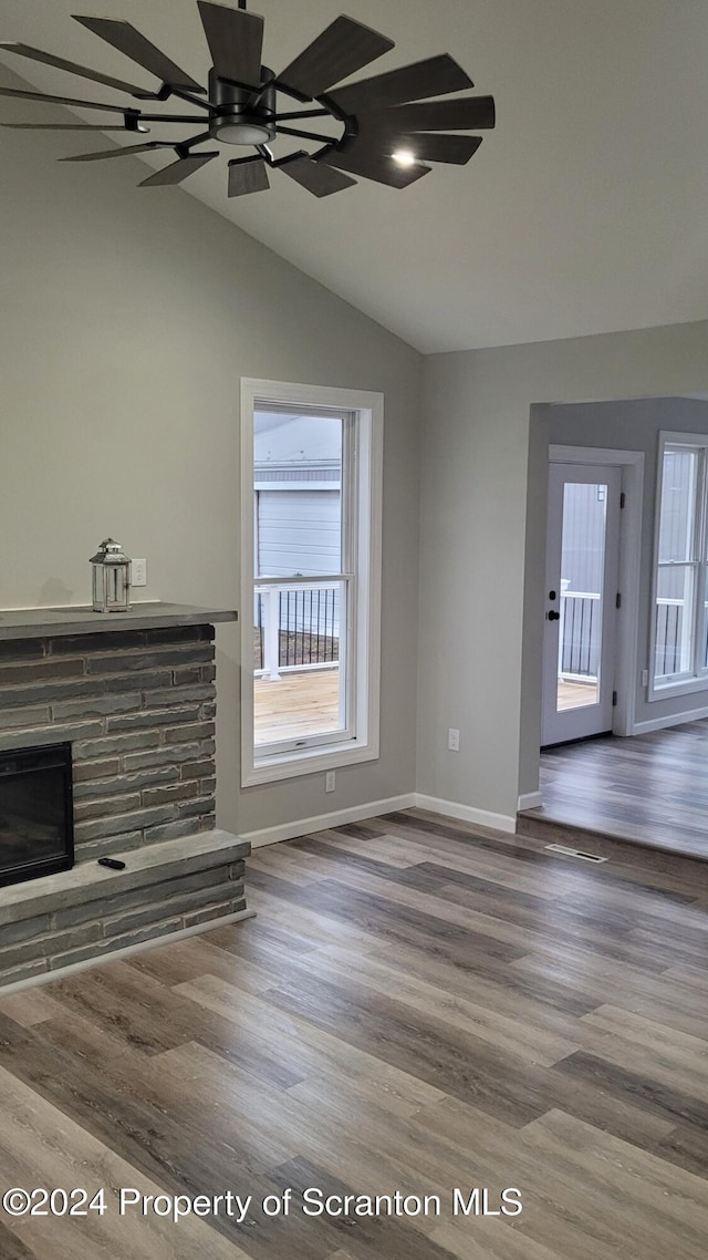 unfurnished living room with hardwood / wood-style flooring, ceiling fan, a stone fireplace, and vaulted ceiling