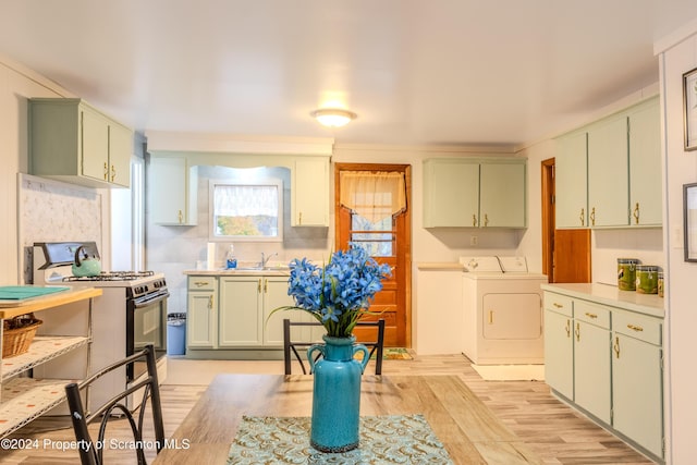 kitchen featuring washer and clothes dryer, sink, green cabinetry, stainless steel range, and light hardwood / wood-style floors