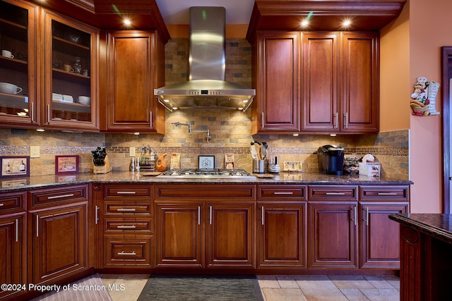 kitchen with wall chimney exhaust hood, dark stone countertops, decorative backsplash, and stainless steel gas cooktop