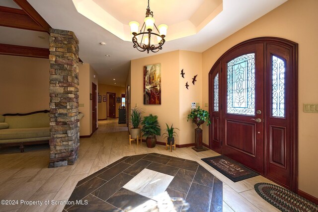 entrance foyer featuring a raised ceiling, ornate columns, and an inviting chandelier