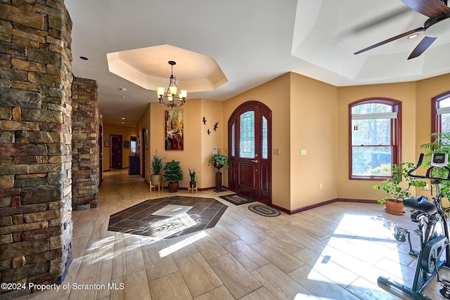 entryway featuring ceiling fan with notable chandelier and a raised ceiling