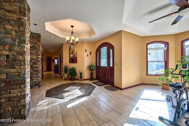 entryway featuring ceiling fan with notable chandelier and a raised ceiling