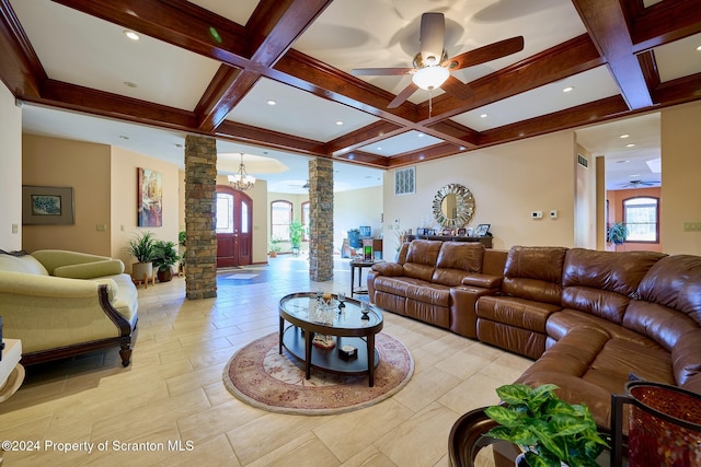 living room featuring beamed ceiling, ceiling fan with notable chandelier, ornate columns, and coffered ceiling