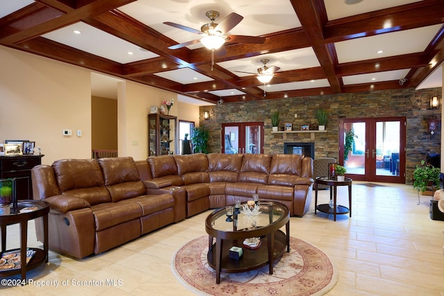 living room with french doors, coffered ceiling, ceiling fan, beam ceiling, and a stone fireplace