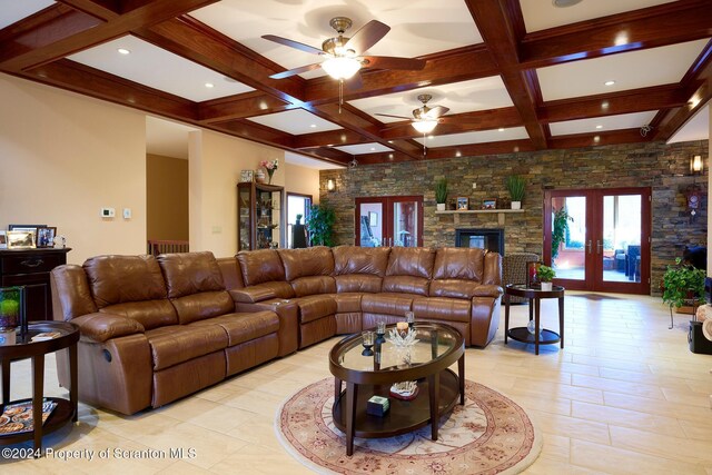 living room with french doors, coffered ceiling, ceiling fan, beam ceiling, and a stone fireplace