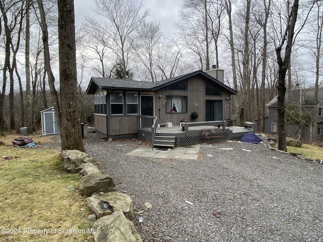 view of front facade with a wooden deck, a sunroom, and a storage shed