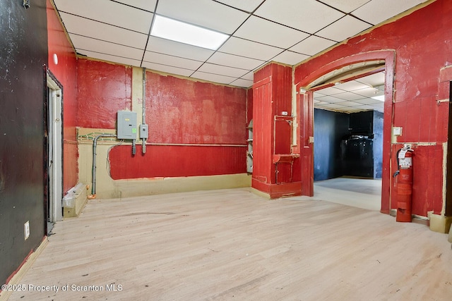 hall with a paneled ceiling, electric panel, and light hardwood / wood-style floors