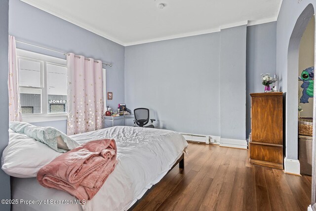 bedroom with ornamental molding, a baseboard heating unit, and wood-type flooring