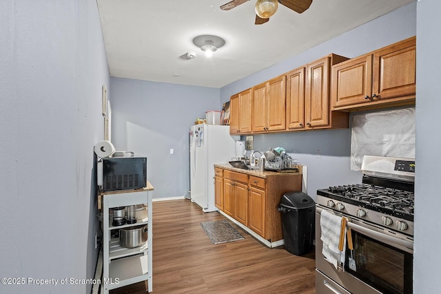 kitchen featuring ceiling fan, sink, white refrigerator, hardwood / wood-style flooring, and stainless steel range with gas stovetop