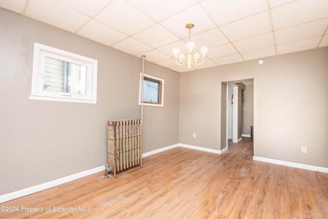 spare room featuring a paneled ceiling, hardwood / wood-style floors, a chandelier, and radiator heating unit