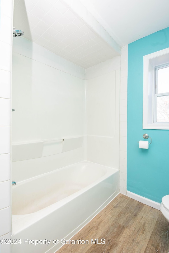 bathroom featuring hardwood / wood-style flooring, toilet, and washtub / shower combination