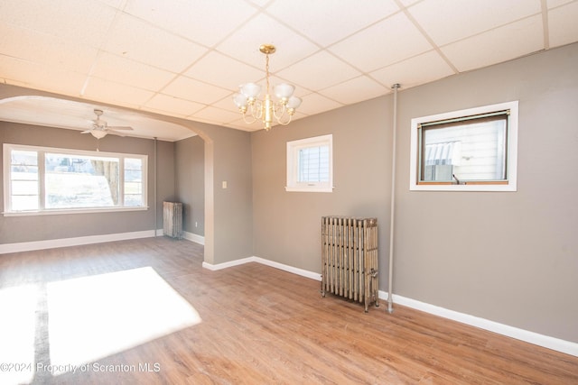 unfurnished room with radiator heating unit, ceiling fan with notable chandelier, hardwood / wood-style flooring, and a drop ceiling