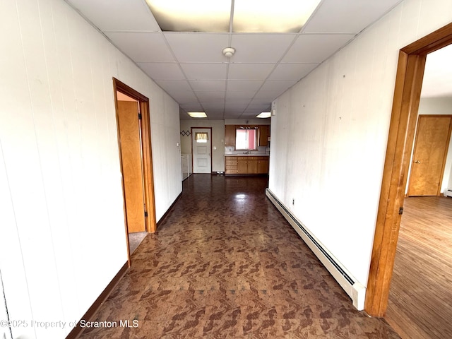 hallway with a drop ceiling, wood walls, and a baseboard radiator