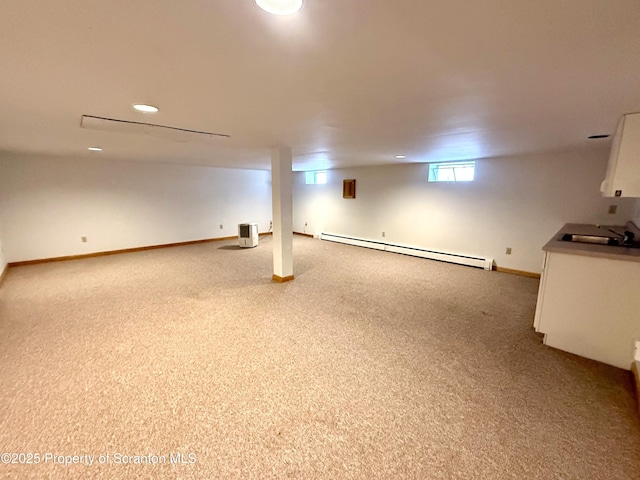 basement featuring light colored carpet, baseboard heating, and sink