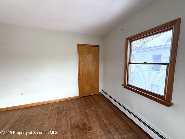 spare room featuring a baseboard heating unit and dark hardwood / wood-style flooring