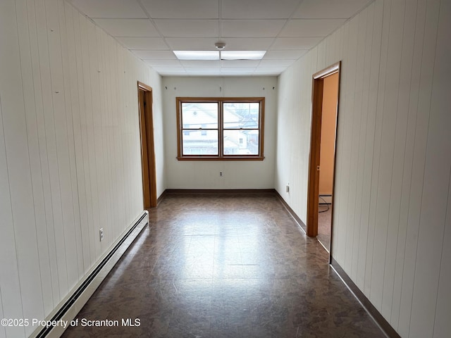 spare room featuring a baseboard heating unit, a drop ceiling, and wood walls