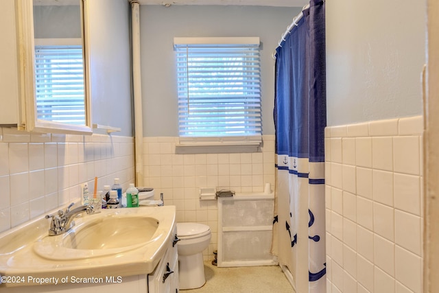 bathroom with a wealth of natural light, vanity, tile walls, and toilet