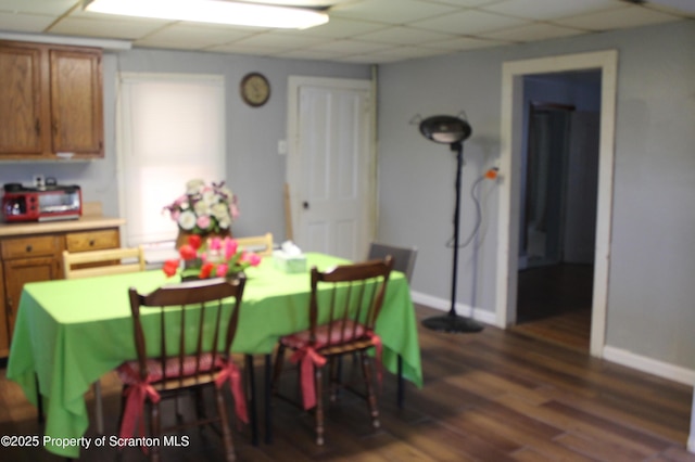 dining room with baseboards, dark wood finished floors, and a drop ceiling