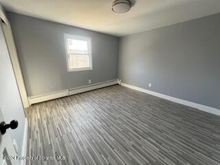 unfurnished room featuring dark hardwood / wood-style floors and a baseboard heating unit