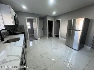 kitchen featuring white cabinets, sink, and stainless steel refrigerator