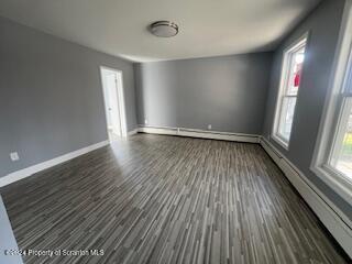 spare room with dark wood-type flooring and a baseboard heating unit