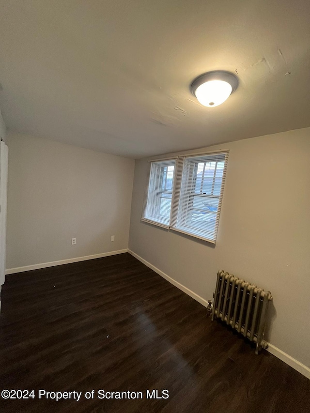 empty room with radiator heating unit and dark hardwood / wood-style flooring