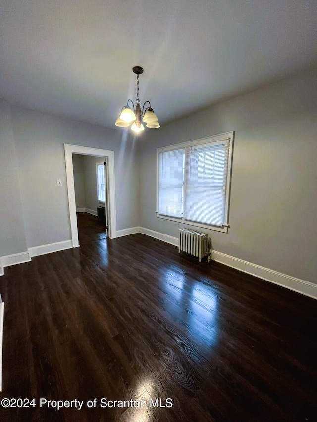 spare room featuring radiator heating unit, dark wood-type flooring, and an inviting chandelier