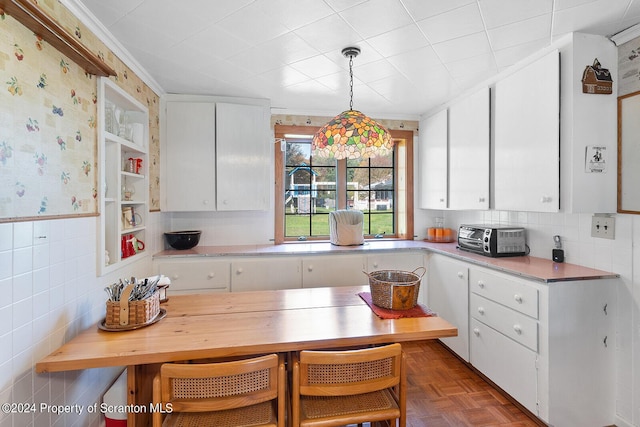 kitchen featuring white cabinetry, dark parquet floors, hanging light fixtures, and ornamental molding