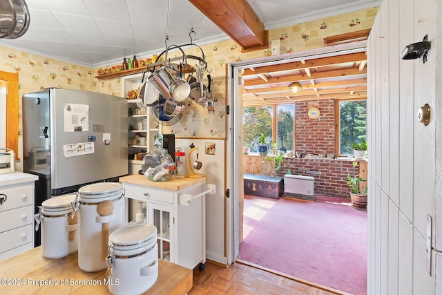 kitchen with beamed ceiling, white cabinetry, light parquet floors, and stainless steel refrigerator