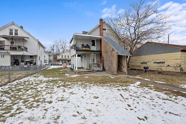 snow covered house with a balcony, a chimney, and fence