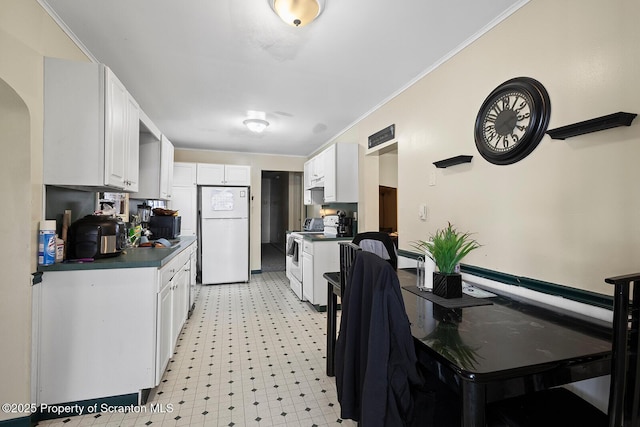 kitchen with white appliances, dark countertops, crown molding, light floors, and white cabinetry