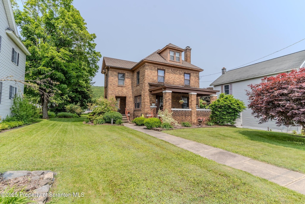 american foursquare style home featuring brick siding, a front lawn, a chimney, and a porch