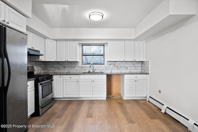 kitchen with a sink, under cabinet range hood, freestanding refrigerator, a baseboard radiator, and stainless steel range with gas stovetop