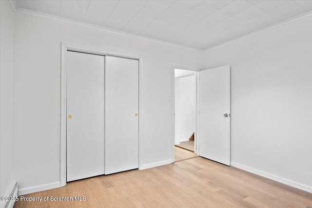 unfurnished bedroom featuring crown molding, light wood-style flooring, baseboards, and a closet