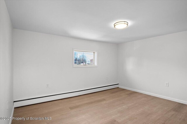 unfurnished room featuring a baseboard heating unit, wood finished floors, and baseboards