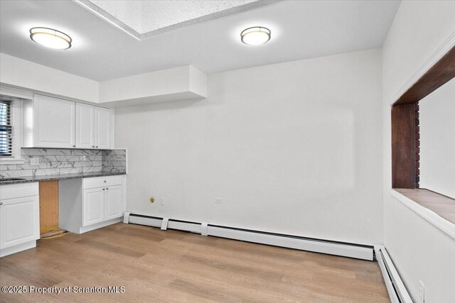kitchen featuring dark countertops, tasteful backsplash, a baseboard heating unit, light wood-type flooring, and white cabinetry