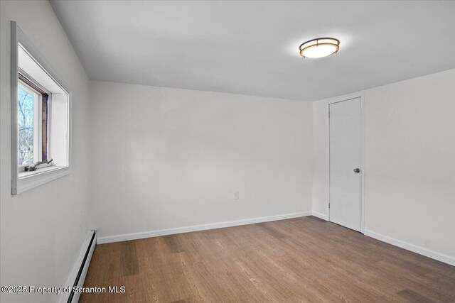 unfurnished room featuring a baseboard radiator, baseboards, and wood finished floors