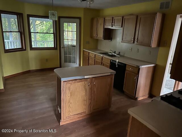 kitchen with dark wood-type flooring, sink, pendant lighting, black dishwasher, and a kitchen island