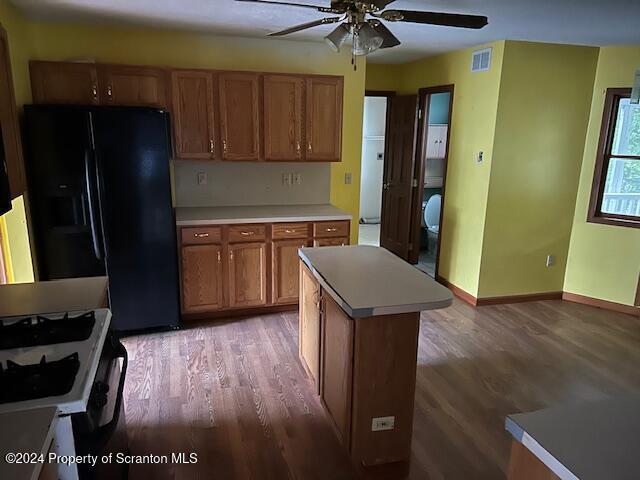 kitchen with black refrigerator with ice dispenser, a center island, wood-type flooring, and white range with gas stovetop