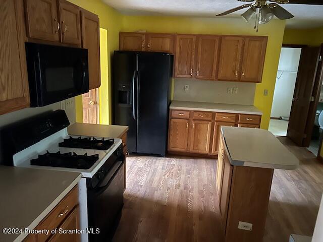 kitchen featuring black appliances, ceiling fan, a kitchen island, and wood-type flooring