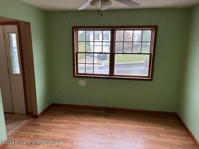 empty room with a textured ceiling, light wood-type flooring, and ceiling fan