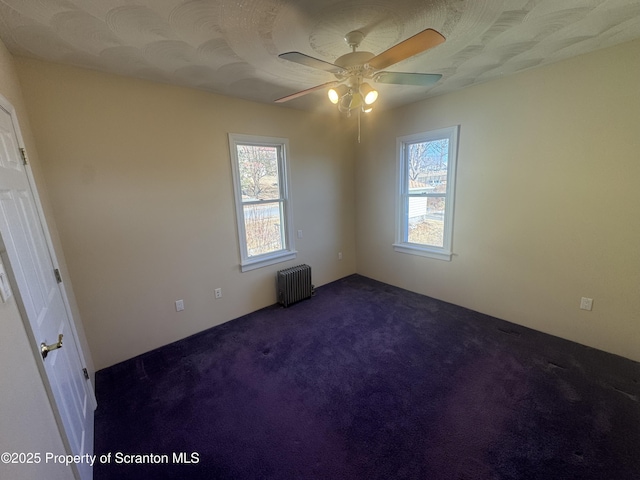 spare room featuring dark colored carpet, ceiling fan, and radiator heating unit