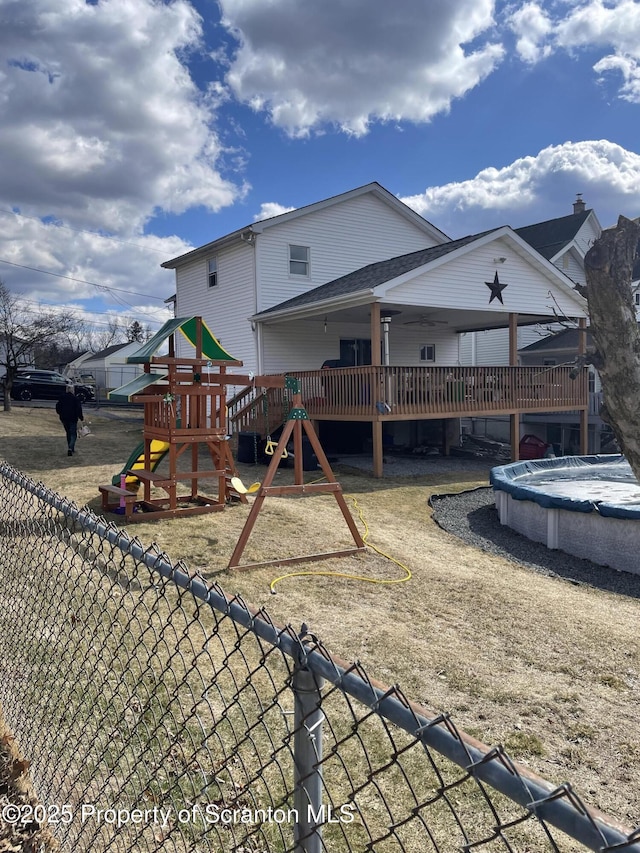 back of house with playground community, a deck, and fence